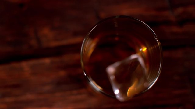 Super slow motion of falling ice cube into whiskey glass, top view. Filmed on cinema slow motion camera, 1000fps