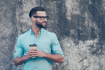 Side view portrait with copyspace of funky macho with modern hairdo having carton cup with coffee in hands looking away isolated on grey stone background. Barista caffeine cafe concept