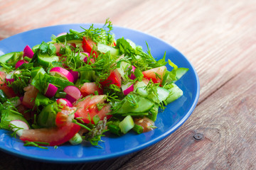 salad of fresh vegetables and greens in a plate on a wooden background