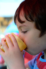 A boy drinking from a plastic beaker.