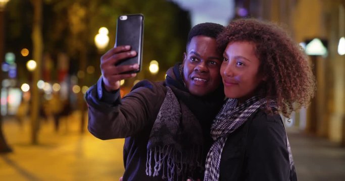 Attractive tourist couple pose for a selfie on the Champs-Elysees at night, Happy millennial black male and female smile for picture on Paris street in evening, 4k