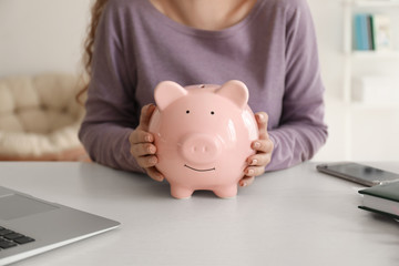 Obraz na płótnie Canvas Young woman holding piggy bank indoors, closeup. Money savings concept