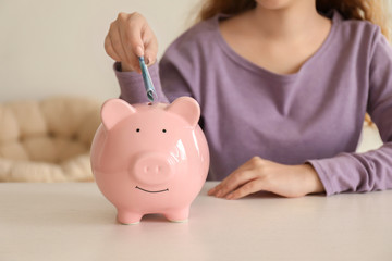 Obraz na płótnie Canvas Young woman putting euro banknote into piggy bank indoors. Money savings concept