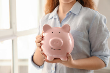 Young woman holding piggy bank indoors. Money savings concept