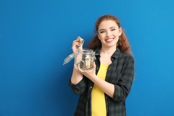 Young woman putting dollar banknote into glass jar with money on color background. Money savings concept