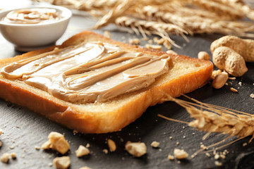 Tasty toast with peanut butter on slate plate, closeup