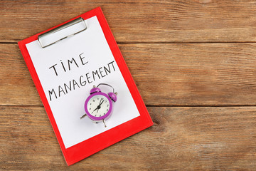 Alarm clock with clipboard on wooden background. Time management concept