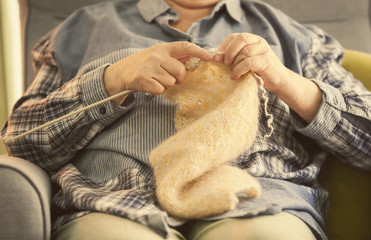 Senior woman sitting on armchair while knitting sweater at home