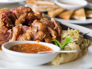 Crispy fried pork leg placed on a plate with vegetables and seasoning sauce