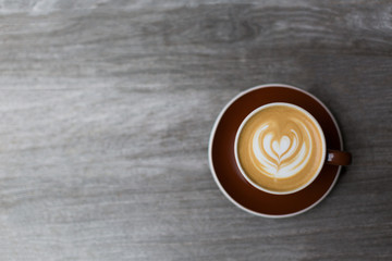 Dark red cup of cappuccino with the heart shape latte-art on wood background