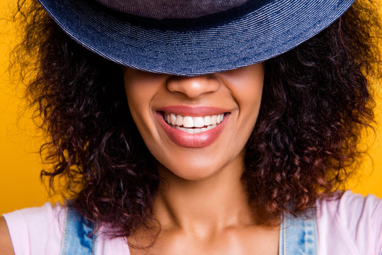 Closeup cropped portrait of cheerful positive girl with white straight teeth hiding half face with hat isolated on yellow background