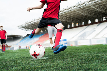 Low section portrait of unrecognizable teenage boy kicking ball forcefully playing football on stadium during practice, copy space