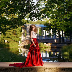 Fashion style photo of young beautiful woman in evening dress with white top and red flying skirt...