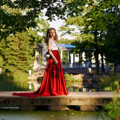 Fashion style photo of young beautiful woman in evening dress with white top and red flying skirt...