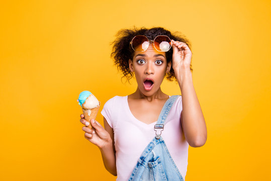 WTF! Portrait of shocked frustrated girl looking out eyeglasses with wide open eyes mouth having ice cream in waffle cone isolated on yellow background
