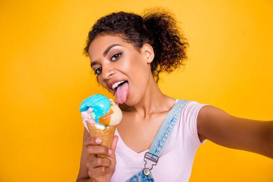 Self portrait of tempting seductive girl having vanilla ice cream in waffle cone licking with tongue out shooting selfie on front camera isolated on yellow background