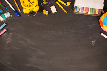 bright office supplies, yellow alarm clock on black chalkboard top view, copy space. concept: back to school, school's out, school holidays, teacher's day