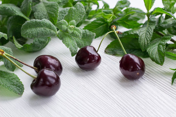 Red cherries, green mint and melissa herbs on white wood