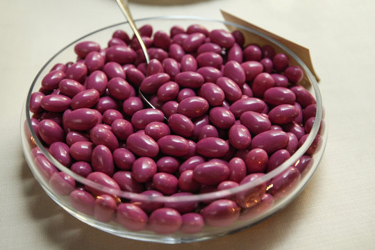 confetti al gusto di frutta color amaranto dentro un largo contenitore in vetro con dentro un cucchiaio