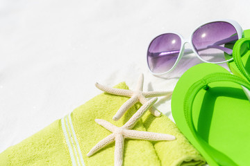 Beach accessories including sunglasses, starfish, colorful flip flop and shell on White sandy beach...