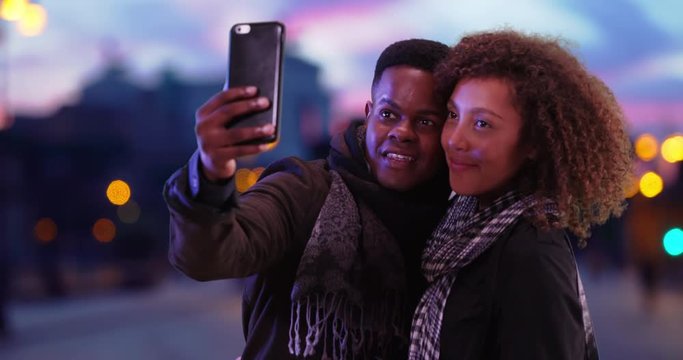 Happy attractive couple pose for selfie on Rome street at night, Black millennial male and female in urban setting take a picture to share on social media, 4k