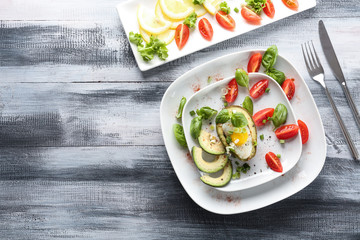 Plate with eggs baked in avocado and fresh vegetables on wooden table