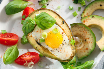 Tasty baked avocado with egg and fresh vegetables on plate, closeup