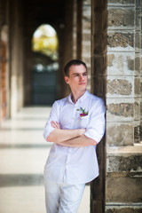 Portrait of the groom in a white shirt near the stone columns of the Catholic Church, who looks to the side