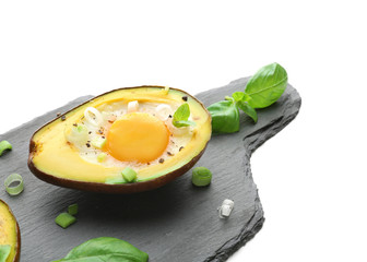 Tasty baked avocado with egg on slate board against white background