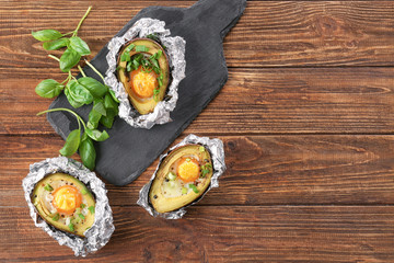 Avocado baked with eggs in foil on wooden table