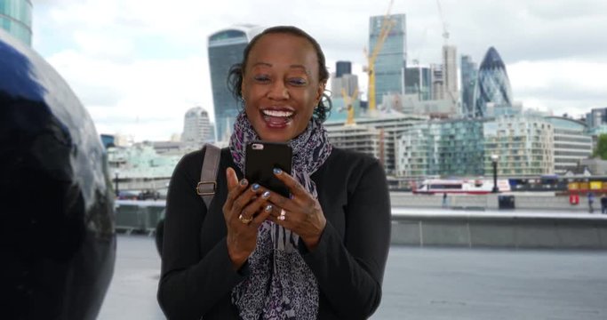 Portrait of elderly black woman laughing at funny text message, Stylish grandma texting on smartphone in downtown London, 4k