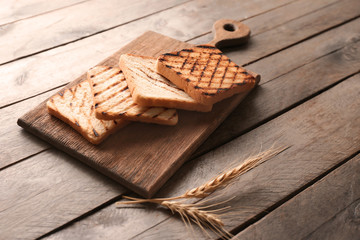 Wooden board with toasted bread on table