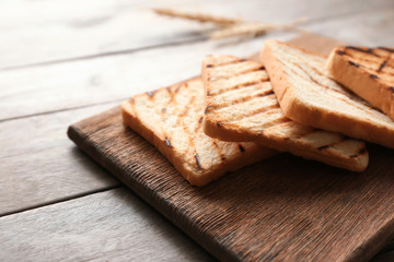 Wooden board with toasted bread on table