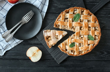Wooden board with tasty homemade apple pie and plate on table