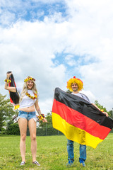 Männlicher und weiblicher Fussballfan jubeln auf Wiese über den Sieg der deutschen Mannschaft