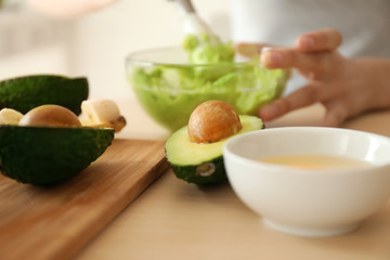 Woman making nourishing mask with avocado in kitchen