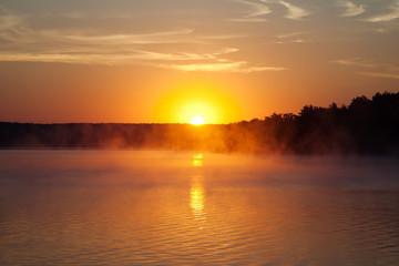 Fototapeta na wymiar Beautiful sunrise on the lake. Early morning landscape. mist on the water, forest silhouettes and the rays of the rising sun.