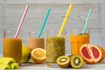 Four glasses of smoothies with straws and various fresh fruits