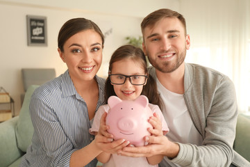 Happy little girl with her parents  holding piggy bank indoors. Money savings concept