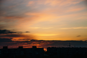 Beautiful cloudy dramatic morning sky above silhouette of city buildings. Picturesque dawn in city. Background of varicolored clouds. Unimaginable fantasy sunrise in heaven.