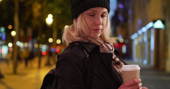 Close-up of white lady wearing beanie and coat looking at camera on sidewalk, Pretty young lady holding coffee and phone looking at camera outside on Champs-Elysees, 4k