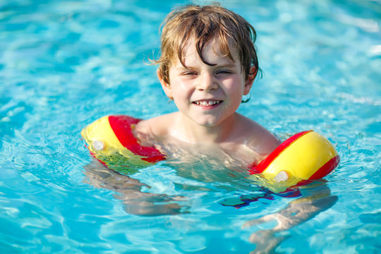 Happy Little Kid Boy Having Fun In An Swimming Pool. Active Happy Preschool Child Learning To Swim. With Safe Floaties