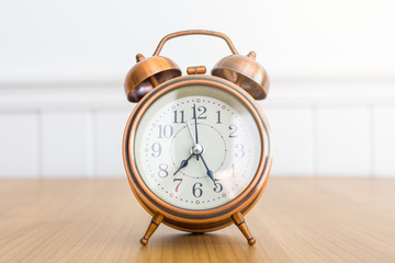 vintage alarm clock on wooden table over white wall background during day