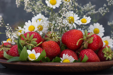 strawberry in a clay dish flowers Gypsophila daisy on a dark gray background close-up.