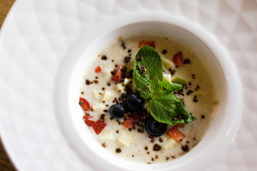 good morning, breakfast and healthy food concept - Tasty oatmeal with strawberries, mint leaves, blueberries and chocolate in white bowl