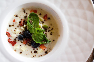 good morning, breakfast and healthy food concept - Tasty oatmeal with strawberries, mint leaves, blueberries and chocolate in white bowl