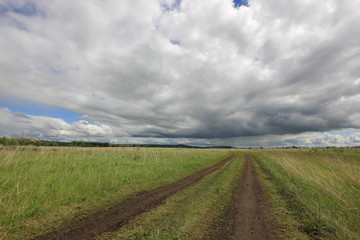 summer landscape with road in the field against the horizon with blue sky and clouds