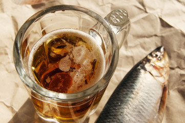 Beer in a glass, a salty herring on paper on a table. Beer and snack to beer.