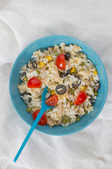 A baby blue bowl with cold rice salad with a spoon.