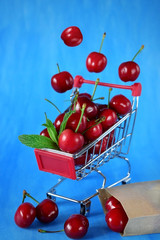 Cherries falling into the shopping cart and scattered around against the blue background